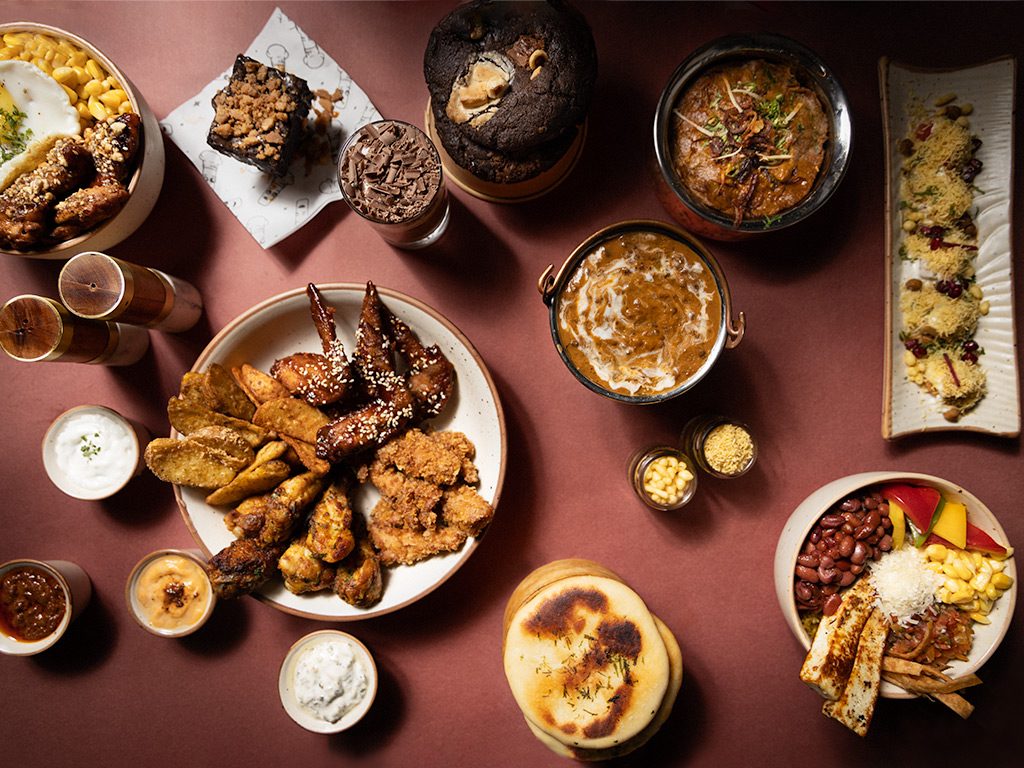 Chef Kenzo editorial flatlay — chicken wings, makhni, sev puri, brownies, naan, rice bowls